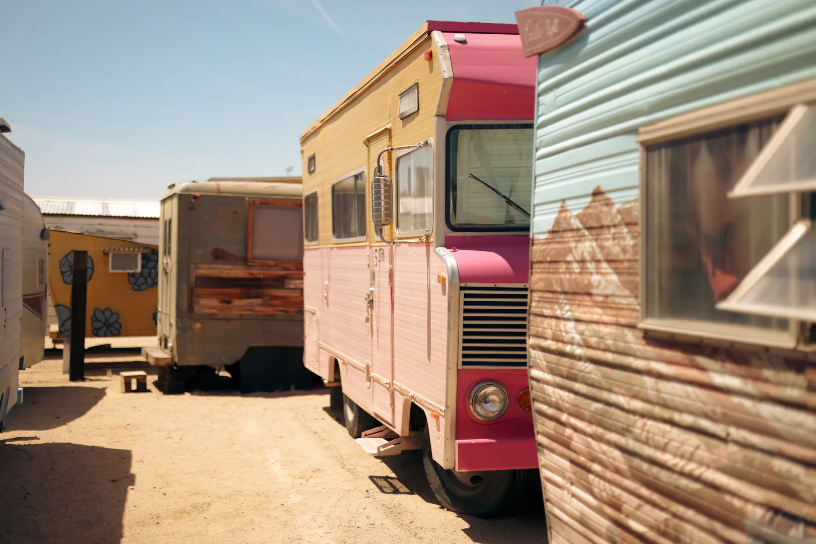 A row of vintage campers parked in full desert sun near Joshua Tree under a clear sky