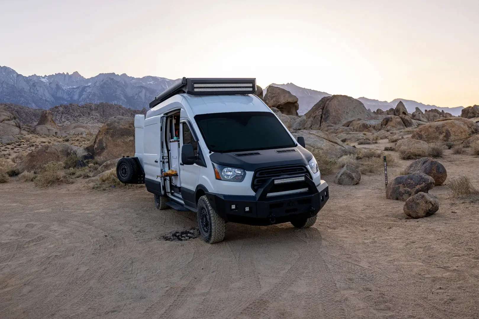 A white camper van parked in open desert sun with rocky mountains behind it, the exact heat problem a battery air conditioner exists to solve