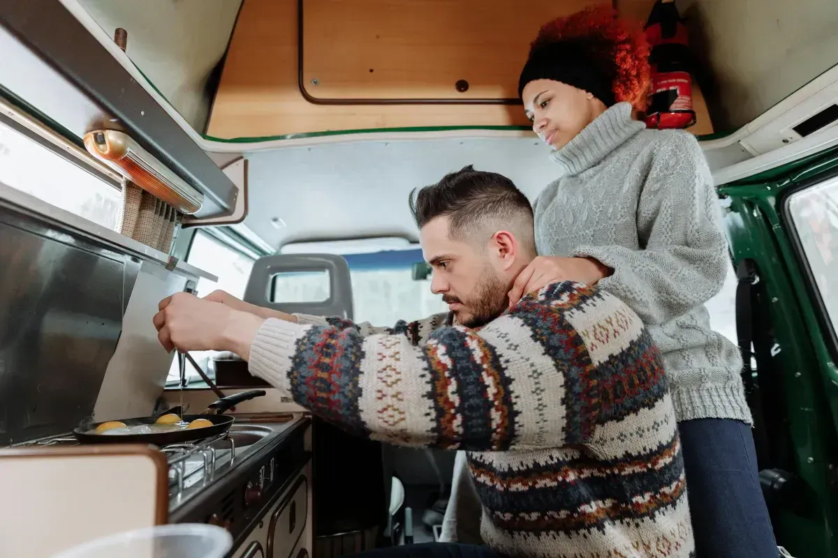 A couple cooking breakfast in the galley kitchen of an off-grid camper van