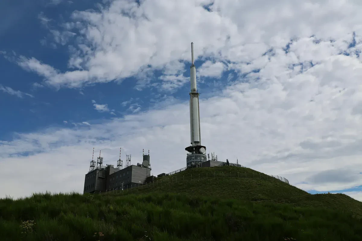 A portable ham radio antenna raised in an open field for off-grid emergency communication, reaching distant repeaters with a clear line of sight