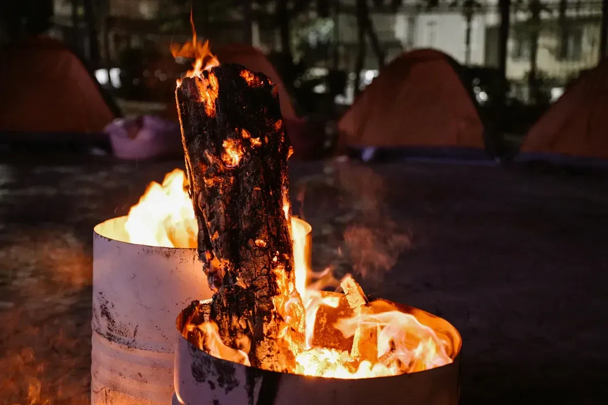 A warm fire glowing among tents at an off-grid campsite at night, evoking propane and camp heat in the dark