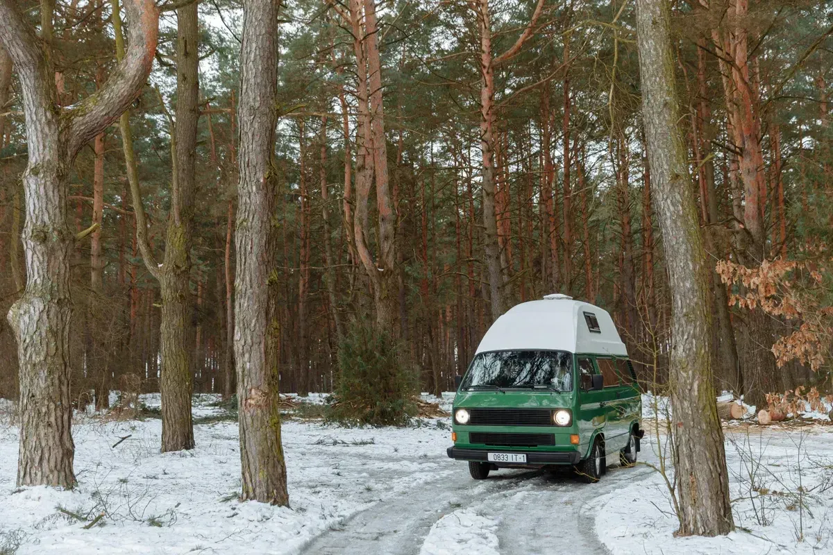 A vintage camper van parked among snow-covered trees in a quiet winter forest, a winter vanlife and off-grid heating scene