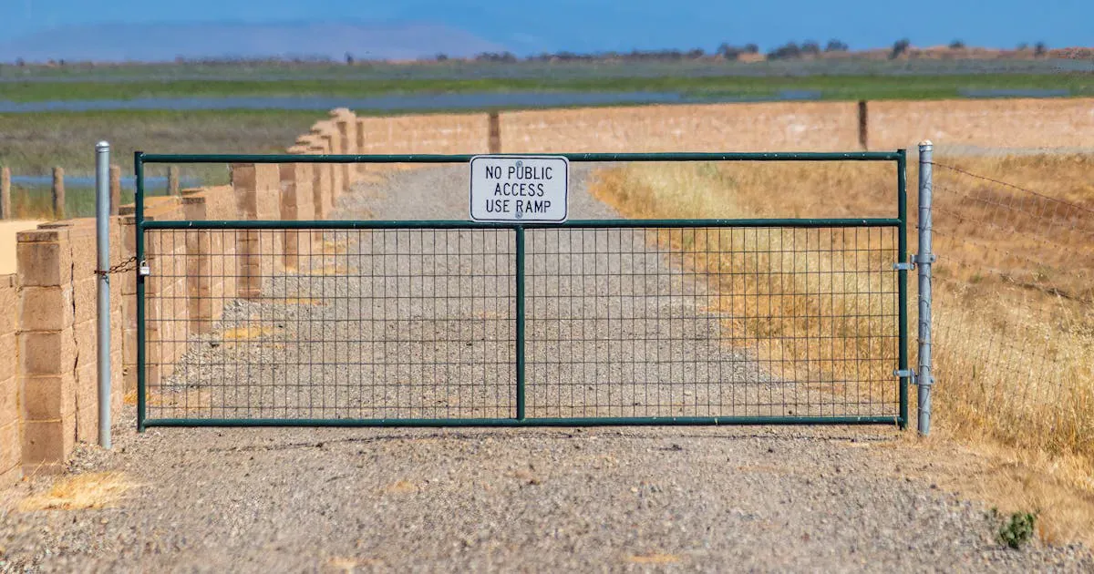 A locked metal gate across a gravel road into the woods, the classic blind spot a cellular security camera covers on remote land
