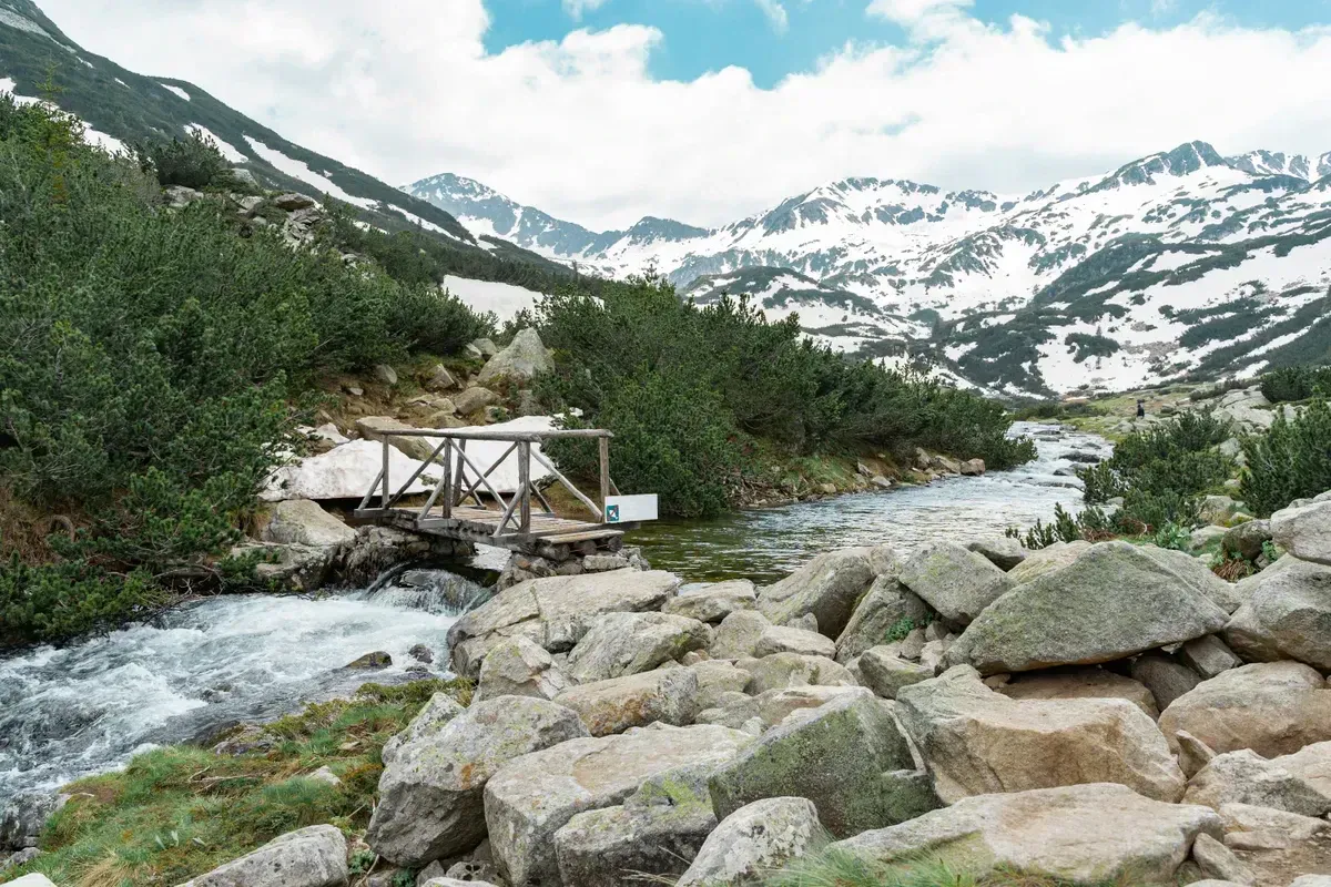 A clear mountain stream flowing past a wooden footbridge through a snowy off-grid wilderness, a natural backcountry water source